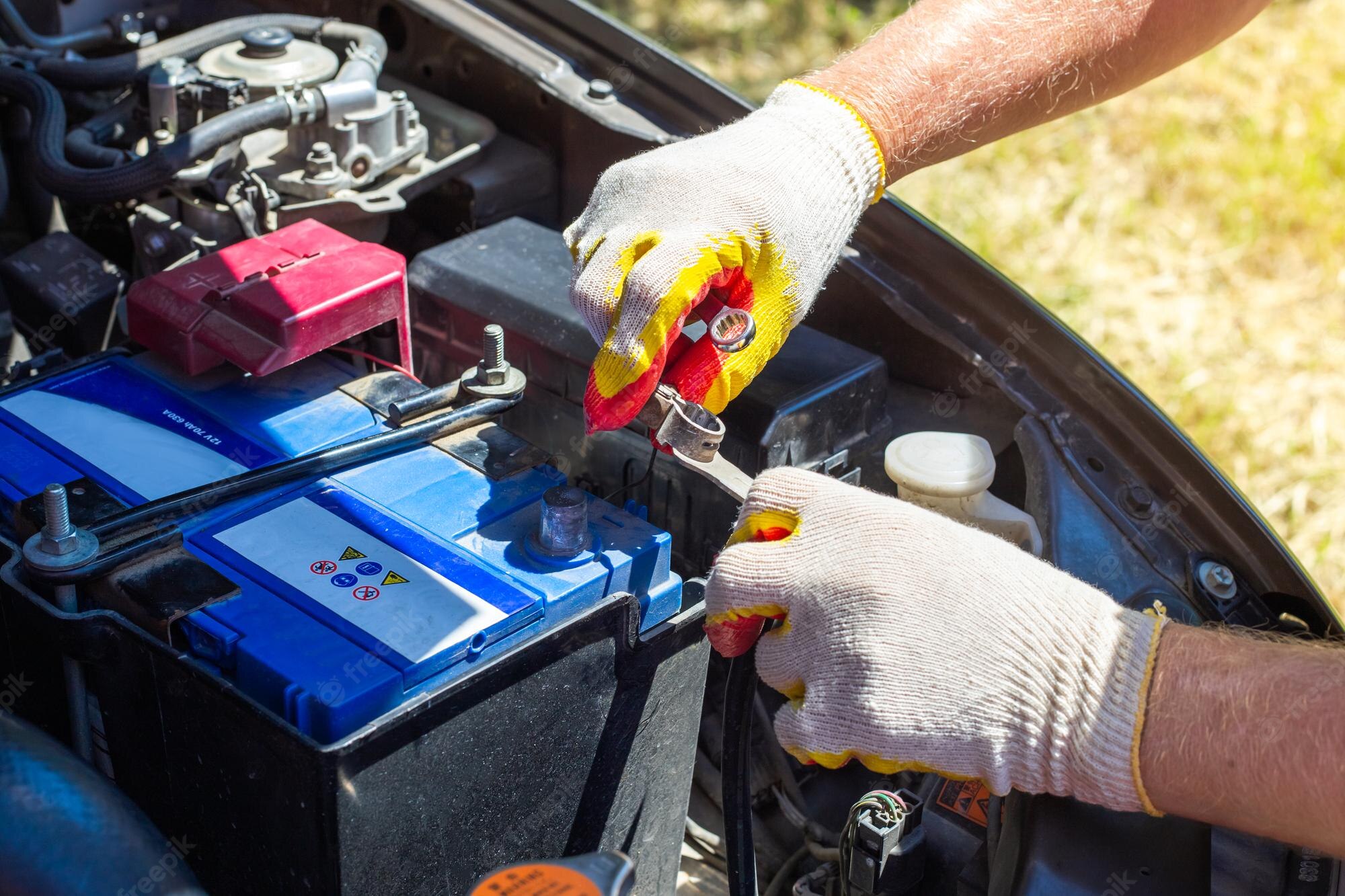Gloved hands using a spanner on the terminal of a car battery under the bonnet